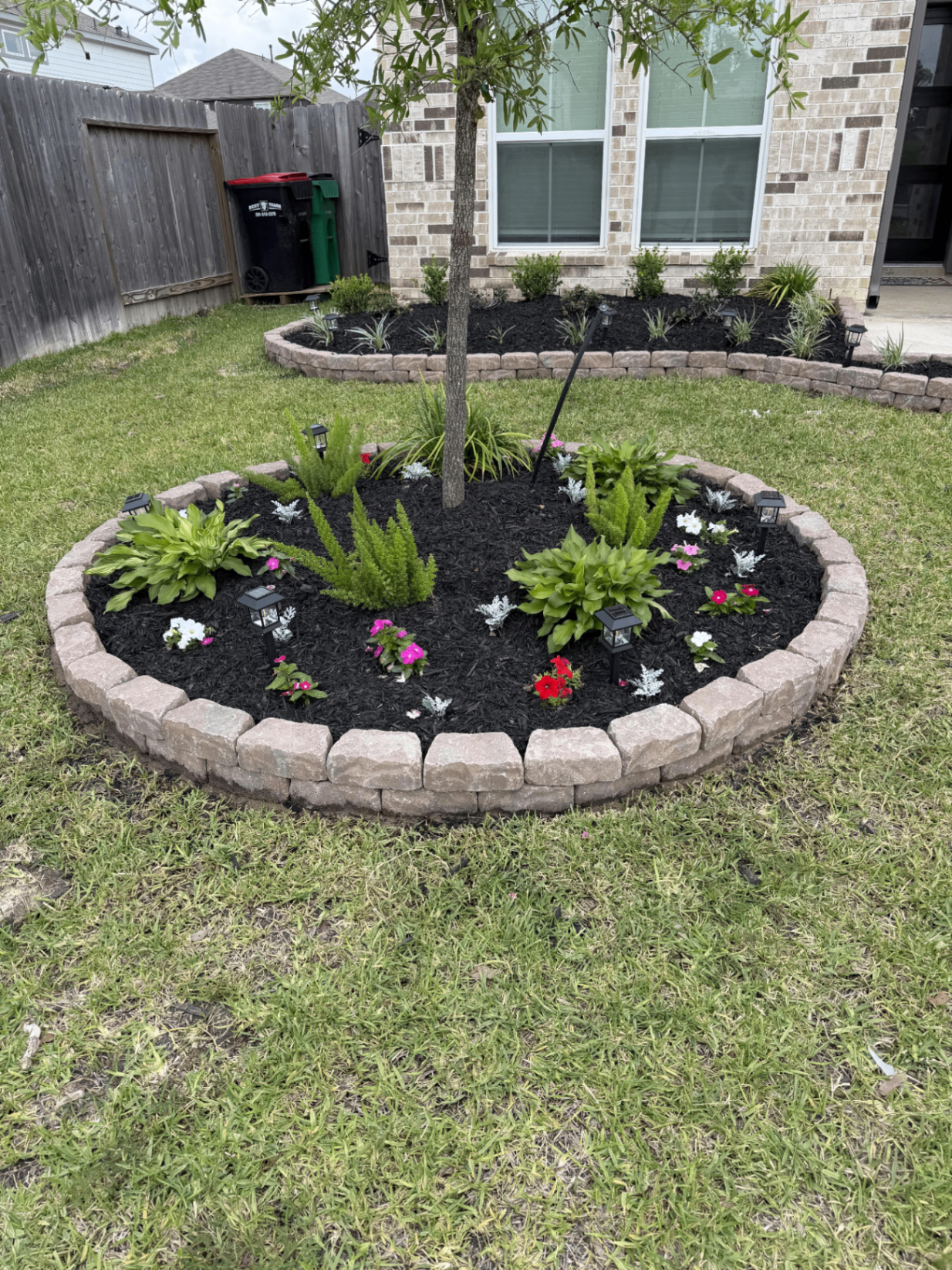 Round stone-edged flower bed with mulch and solar lights