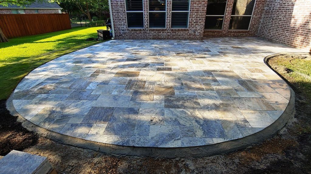 Curved travertine paver patio behind brick home
